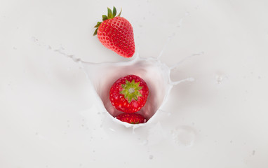 Strawberries falling into milk