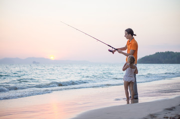 Father with adorable daughter fishing with rod on ocean beach on