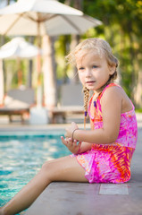 Naklejka premium Adorable girl seat on pool side at tropical beach with legs in