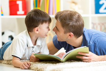 father and his kid son reading a book on floor at home