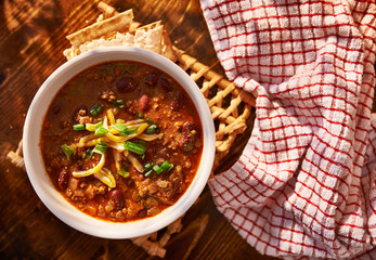 overhead photo of a bowl of chili with cheese and green onions