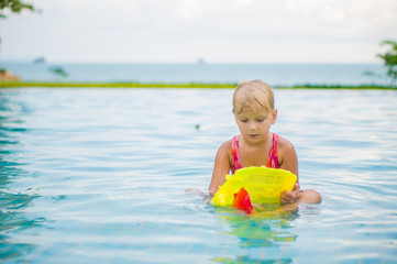 Adorable girl seat and play with toy boat in pool at tropicapl b