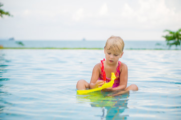 Adorable girl seat and play with toy boat in pool at tropicapl b