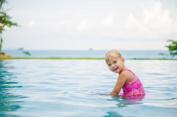 Adorable girl seat and look to camera in pool at tropicapl beach