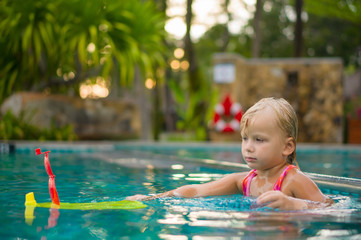 Adorable girl stay near pool side and play with toy boat in pool