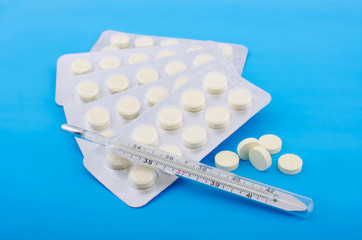 Таблетки и градусник на голубом фоне