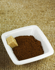 ceramic bowl with ground coffee and brown sugar cube on texture