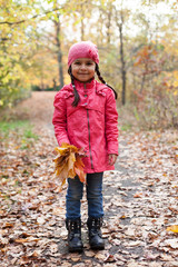 Little pretty girl with autumn leaves in an autumn park