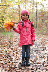 Little pretty girl with autumn leaves in an autumn park