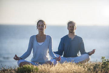 handsome couple practicing meditation exercises on the beach at
