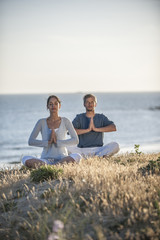 Fototapeta premium handsome couple practicing meditation exercises on the beach at