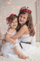 Girl hugs her little sister, both wearing red Christmas caps and
