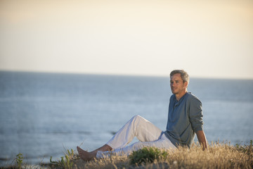 Naklejka na ściany i meble handsome man sitting on the beach at sunset