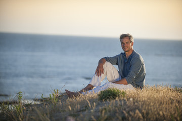 Naklejka na ściany i meble handsome man sitting on the beach at sunset