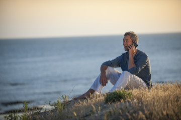 handsome man at phone sitting on the beach at sunset