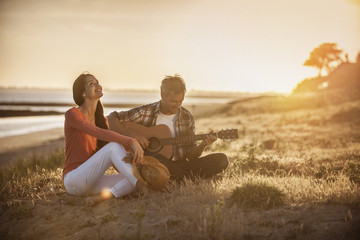 Romantic couple sitting on the beach at sunset with the man play