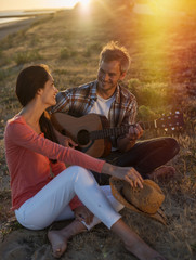 Romantic couple sitting on the beach at sunset with the man play