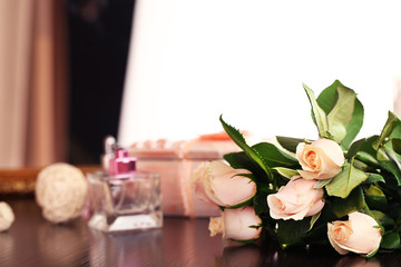 Beautiful roses, perfumes on table near mirror