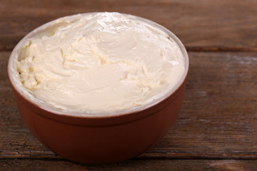 Fresh homemade butter in bowl, on wooden background