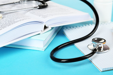 Medical stethoscope with notepad and books on blue background