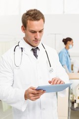 Doctor using digital tablet with colleagues and patient behind