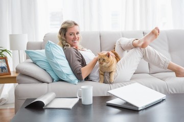 Cheerful woman lying on sofa cuddling a ginger cat