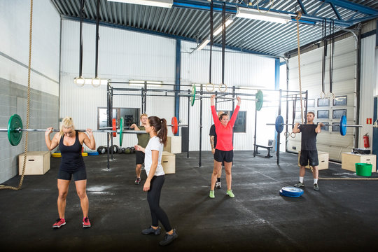 Trainer Assisting Athletes In Lifting Barbells