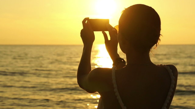 Woman taking pictures with her smartphone at sunset