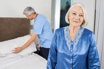 Obraz premium Senior Woman With Caretaker Making Bed At Nursing Home