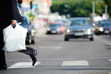 Obraz premium Man in suit with plastic bag crossing street