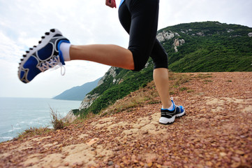 young fitness woman legs running on seaside mountain trail 