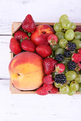 Different berries and fruits in box on wooden table close-up