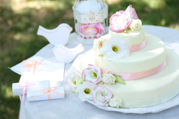 Beautiful wedding cake with flowers on table, outdoors