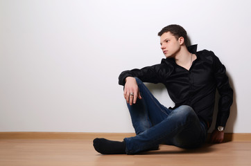 Fashion portrait of young man in black shirt poses over wall