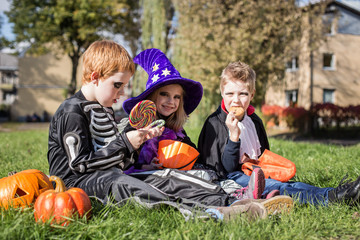 Fototapeta premium cute friends sitting on the grass and eating Halloween candies