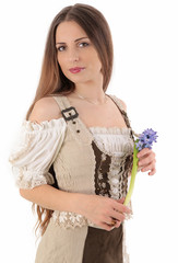 Ein h&uuml;bsches, br&uuml;nettes M&auml;dchen mit langen Haaren im Dirndl h&auml;lt einen Strau&szlig; lila Feldblumen (Muscari neglectum) in der Hand