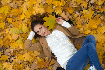 Young beautiful girl in blue jeans lying on yellow leaves