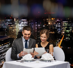 couple with menus on tablet pc at restaurant