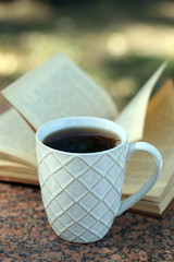 Cup with hot drink and book, outdoors