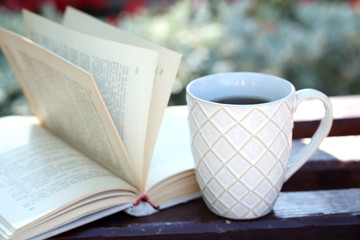 Cup with hot drink and book on bench, outdoors