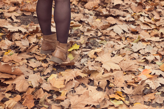womean's feet in boots with autumn leaves on the ground