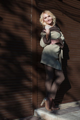 Fototapeta na wymiar beautiful blonde in the coat stands near a wall