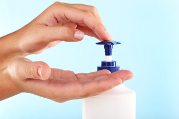 Female hands using liquid soap on light blue background