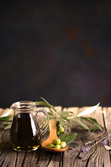 A jar of olive oil and a wooden spoon with olives on a table