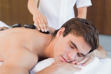 Fototapeta na wymiar Young man receiving stone massage at spa center