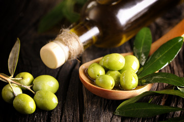 Olive oil and green olives on a wooden spoon