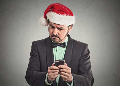skeptical man wearing santa claus hat looking at smartphone