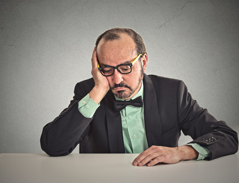 Desperate businessman sitting leaning on a desk looking down