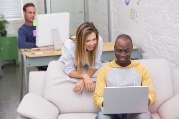 Casual colleagues using laptop on couch in office