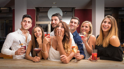 Young friends having fun in a bar drinking cocktail while watchi